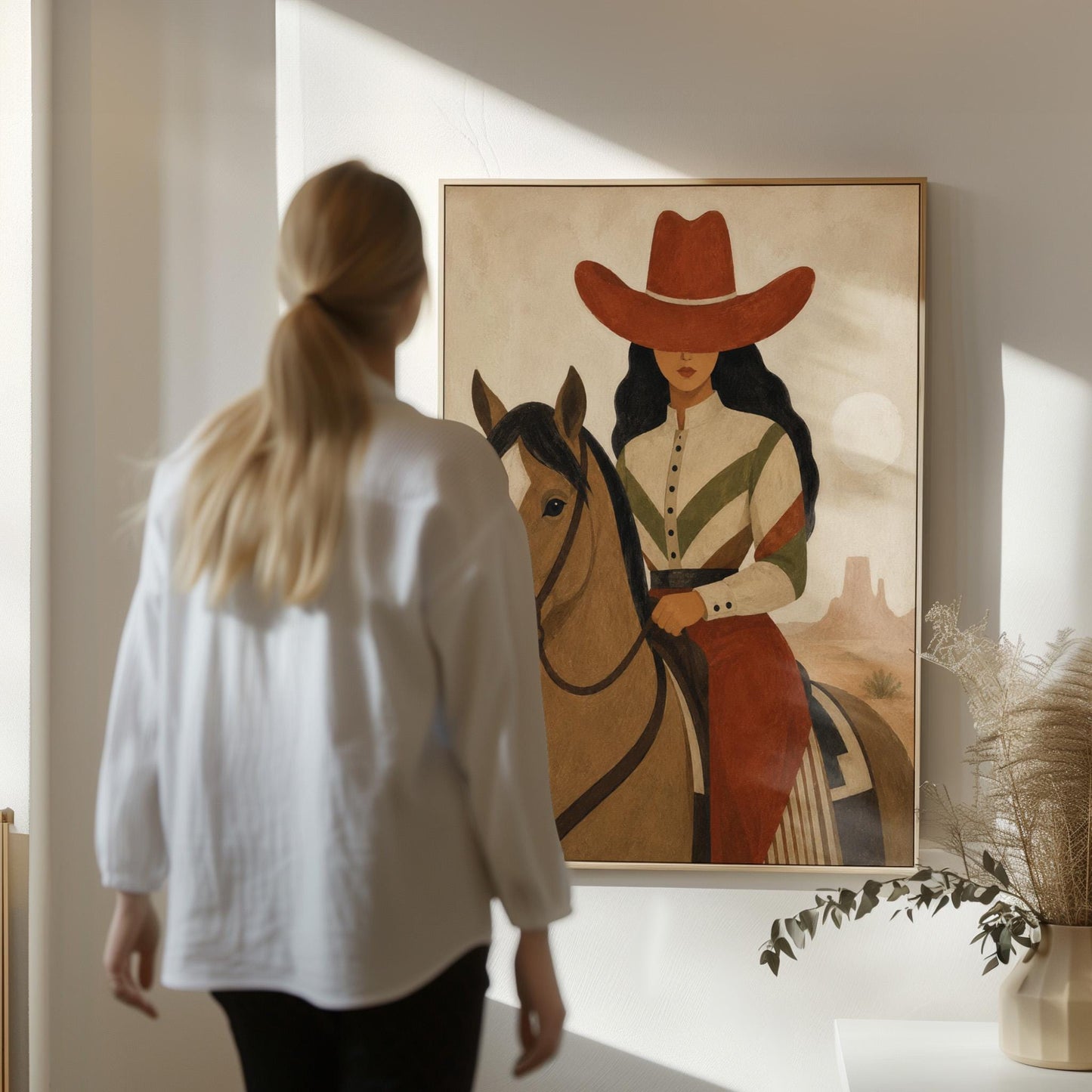 Cowgirl in a red hat riding a bay horse across an ochre desert, canvas wall art styled against a soft white wall
