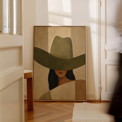 Cropped cowgirl face beneath the sweeping brim of a large olive hat, canvas print shown in a sunlit, contemporary room