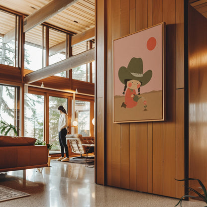 Cowgirl in a green hat watering a small flower in the desert, canvas print shown to scale in a furnished room