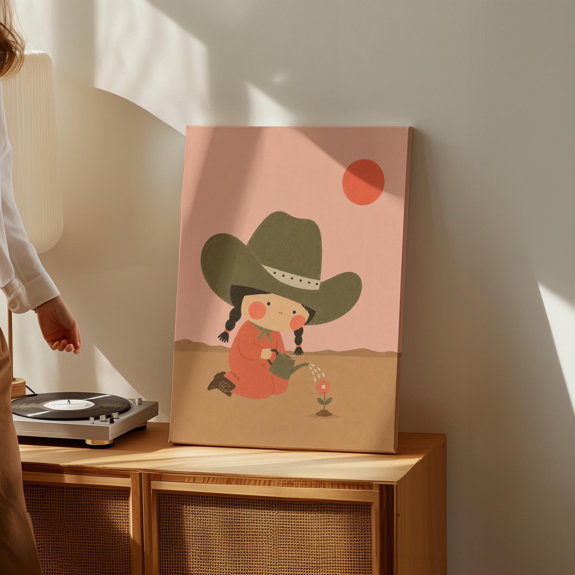 Cowgirl in a green hat watering a small flower in the desert, canvas wall art on a quiet wall in a considered interior