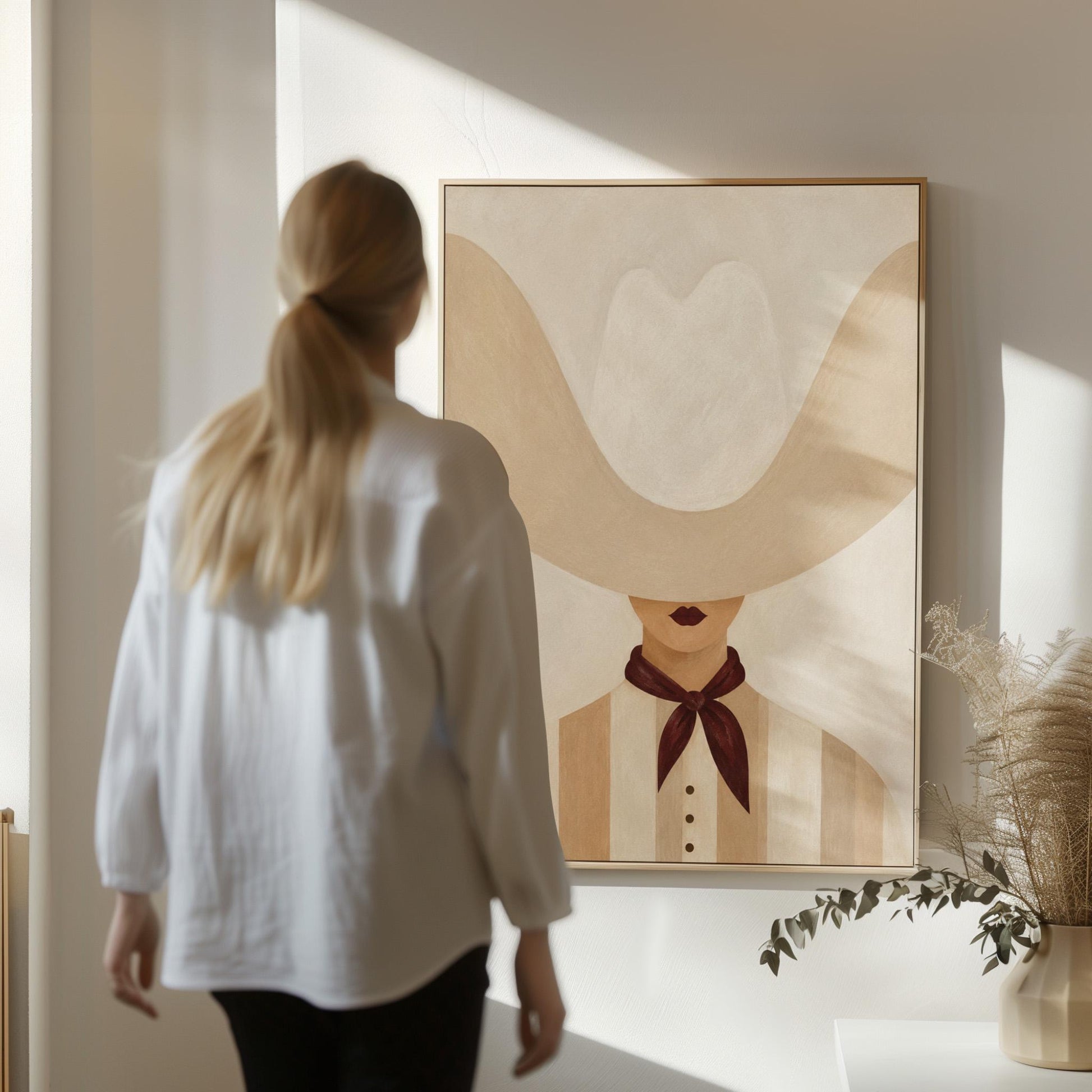 Woman under an oversized pale cowboy hat with a plum neckerchief, canvas wall art seen in a warm interior with natural light