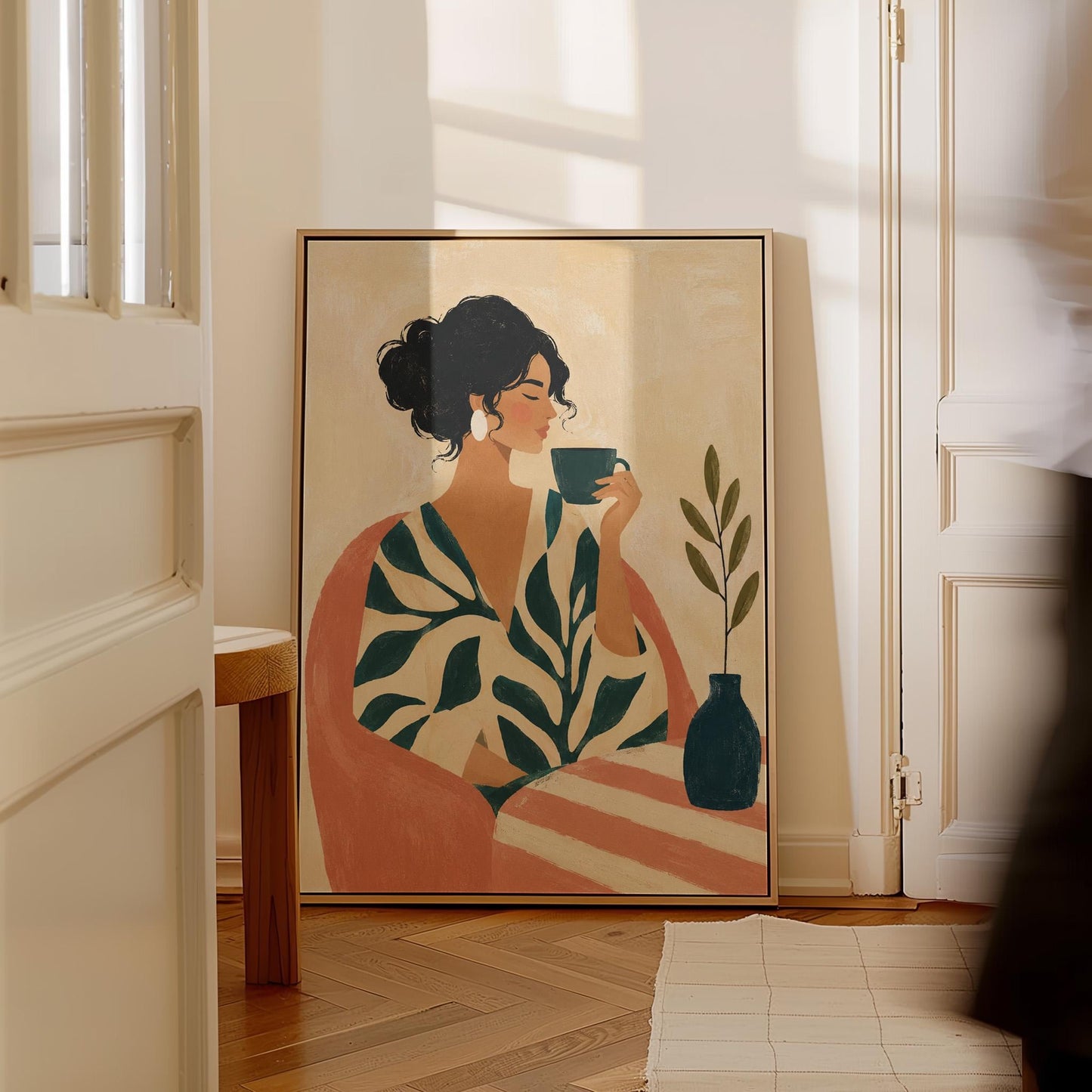 Woman in a leaf print robe drinking from a teal cup beside a vase, canvas print shown to scale in a furnished room