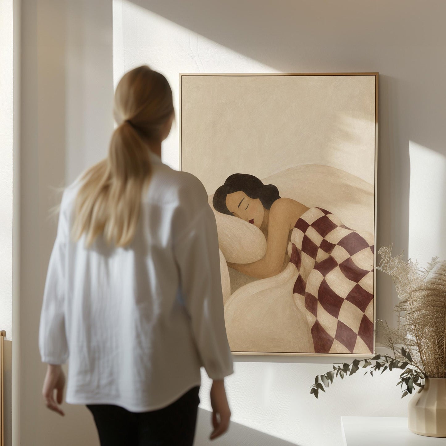 Woman sleeping under a burgundy and cream checkerboard blanket, canvas print presented in a light, minimal room