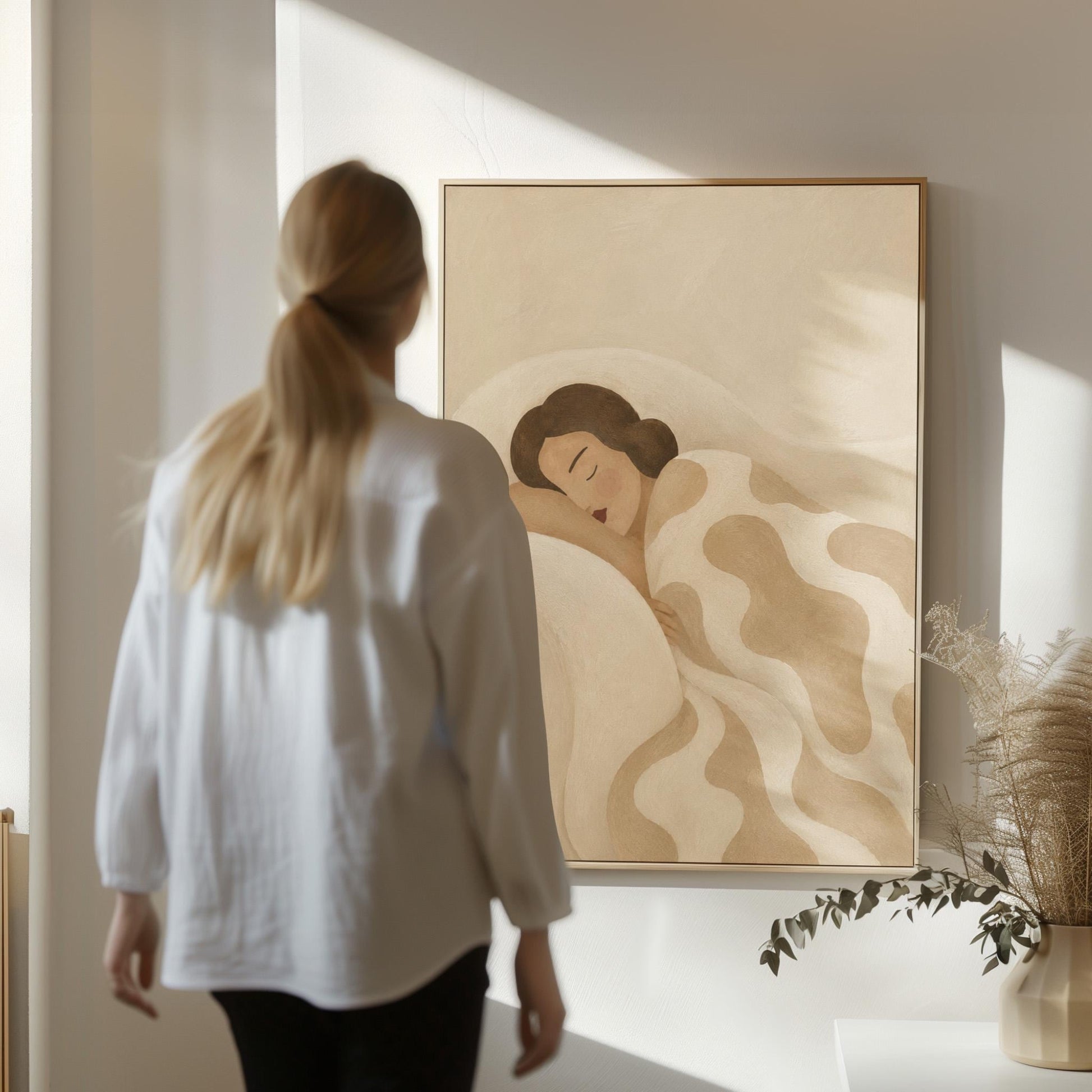 Woman sleeping under a cream blanket with soft camel cloud shapes, canvas print presented in a light, minimal room