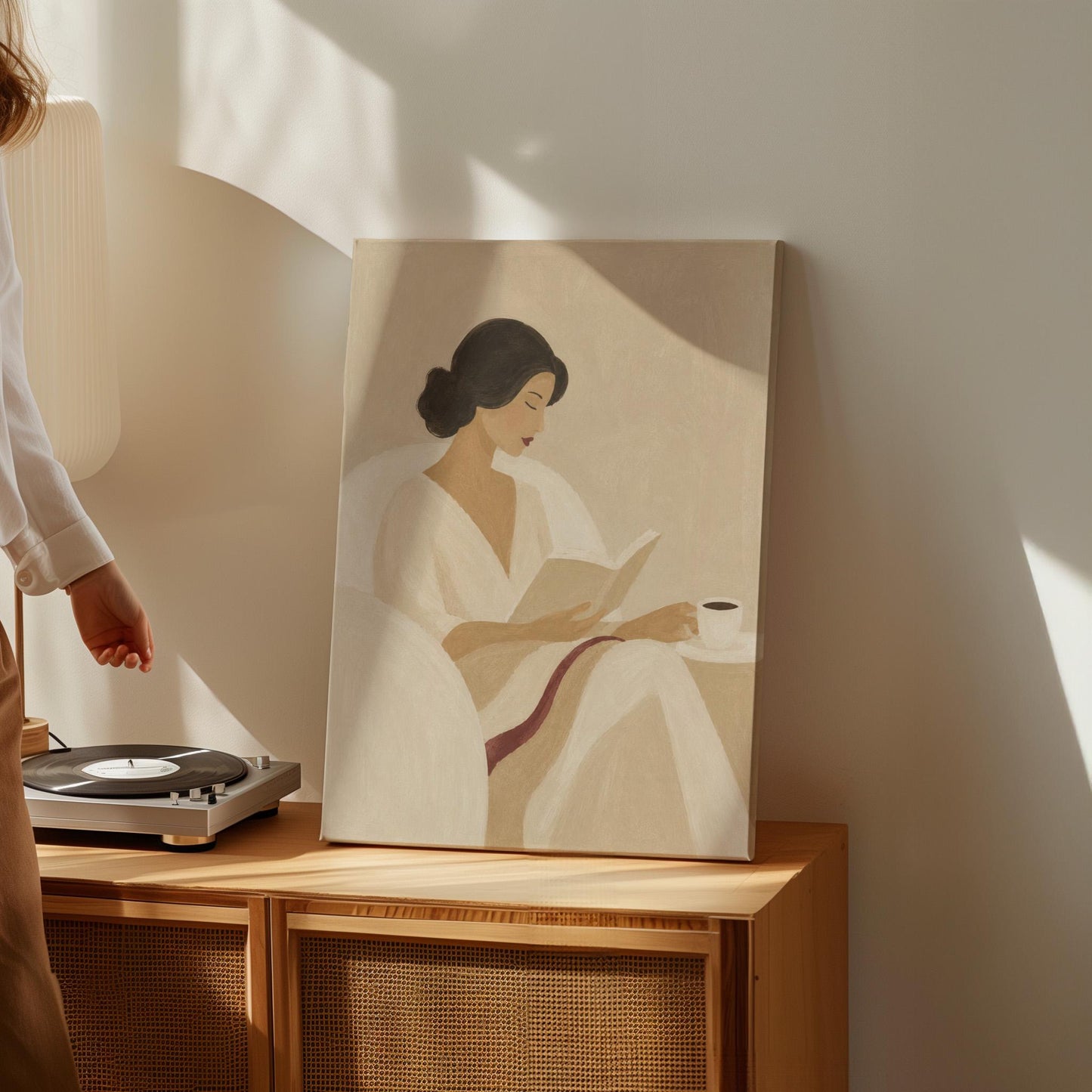 Woman in a white robe reading in an armchair with a black coffee, canvas print displayed on a neutral wall in a styled interior