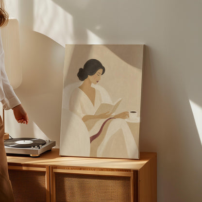 Woman in a white robe reading in an armchair with a black coffee, canvas print displayed on a neutral wall in a styled interior