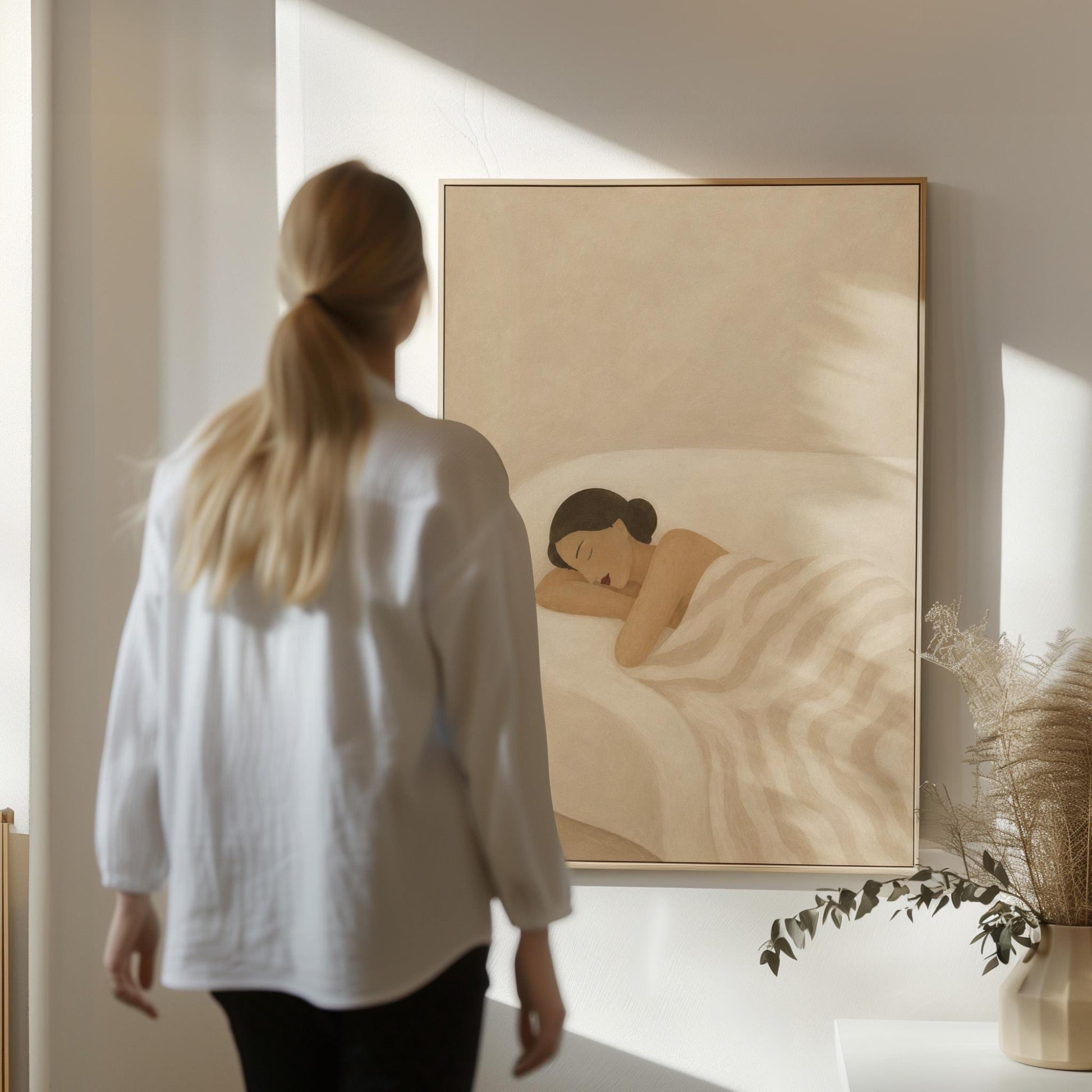 Woman sleeping with hands under her cheek beneath a soft striped quilt, canvas print displayed on a neutral wall in a styled interior