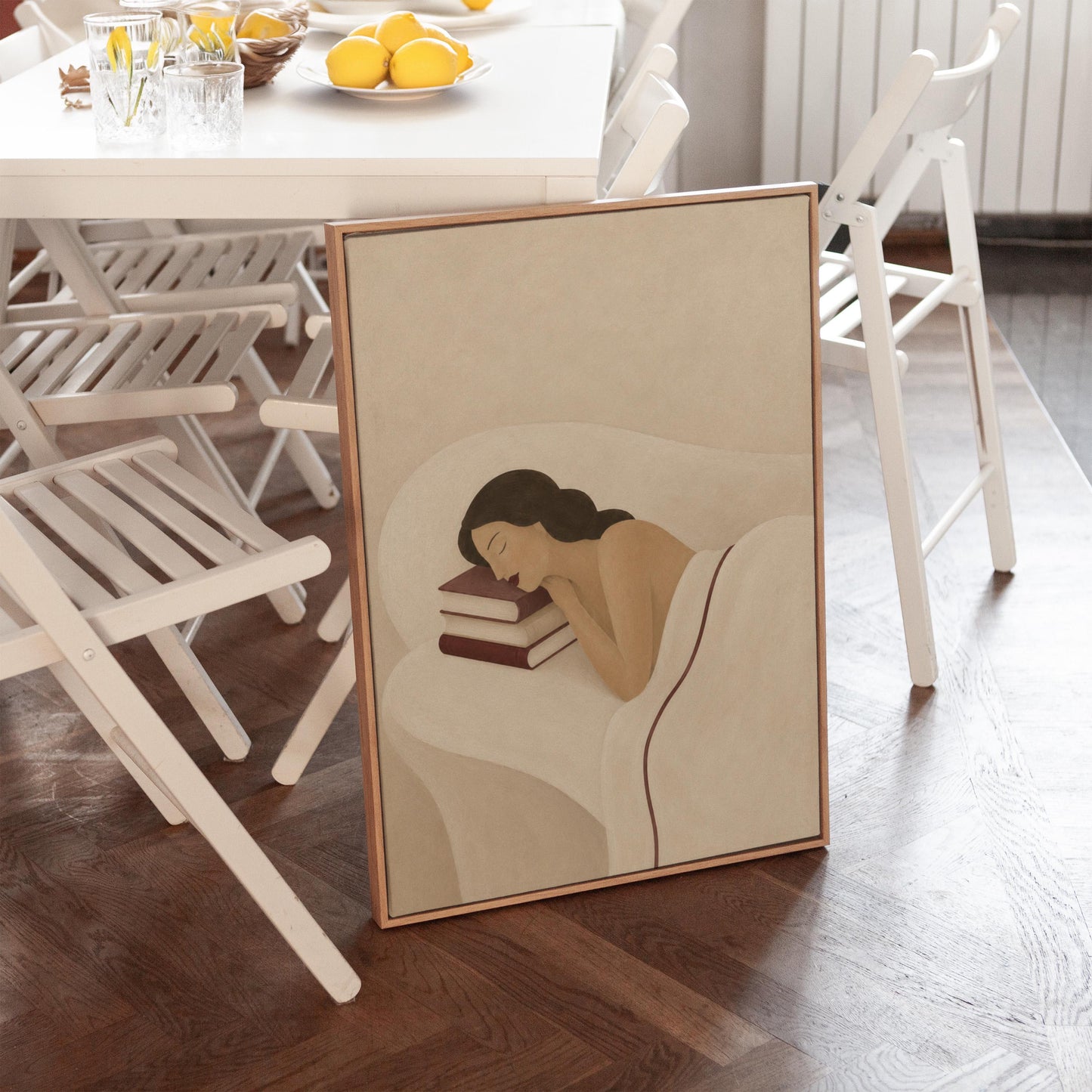 Woman resting her cheek on a stack of cream and burgundy books, canvas wall art styled against a soft white wall