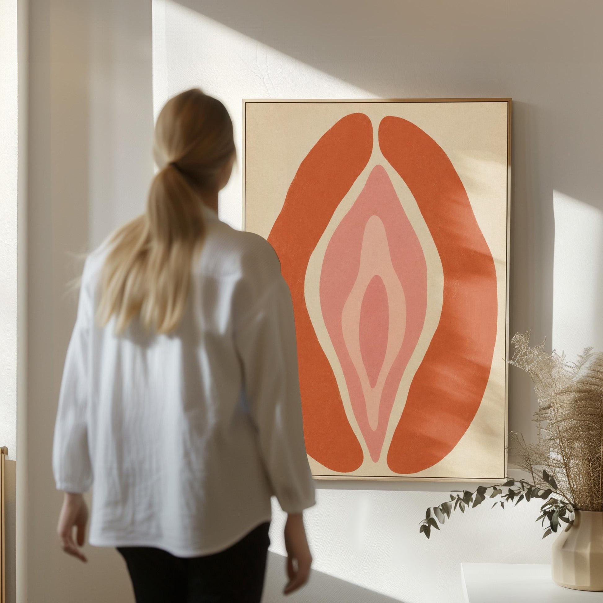 Rust orange arcs curving around a nested blush pink core on sand, canvas print shown to scale in a furnished room