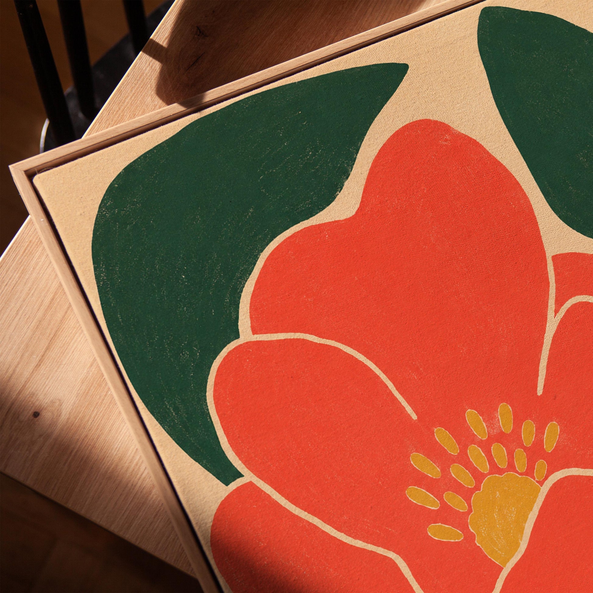 Scarlet flower with gold stamens over deep green leaves on sand, canvas print in a warm, minimally styled interior
