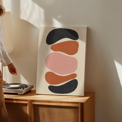 Five stacked pebble shapes in charcoal rust and blush on cream, canvas print displayed on a neutral wall in a styled interior