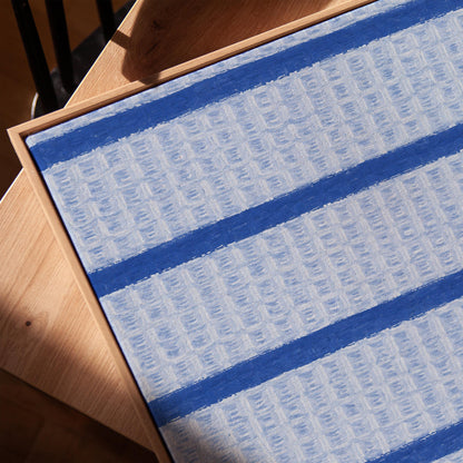Bold cornflower blue stripes on a pale blue background, canvas print in a warm, minimally styled interior