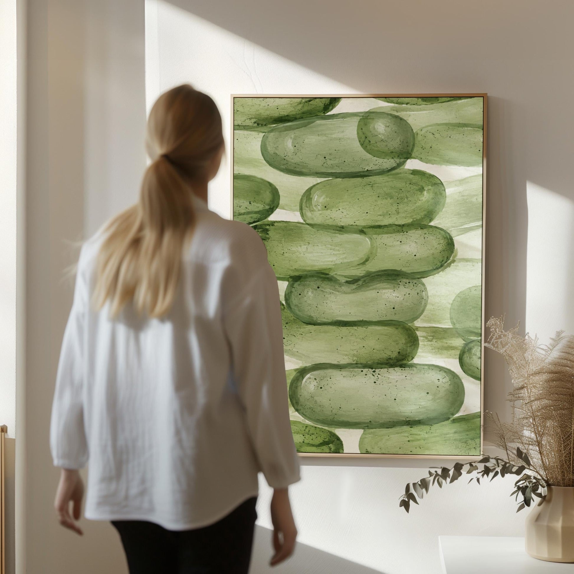 Stacked smooth green stones painted in watercolor, canvas print seen in a warm interior with natural light