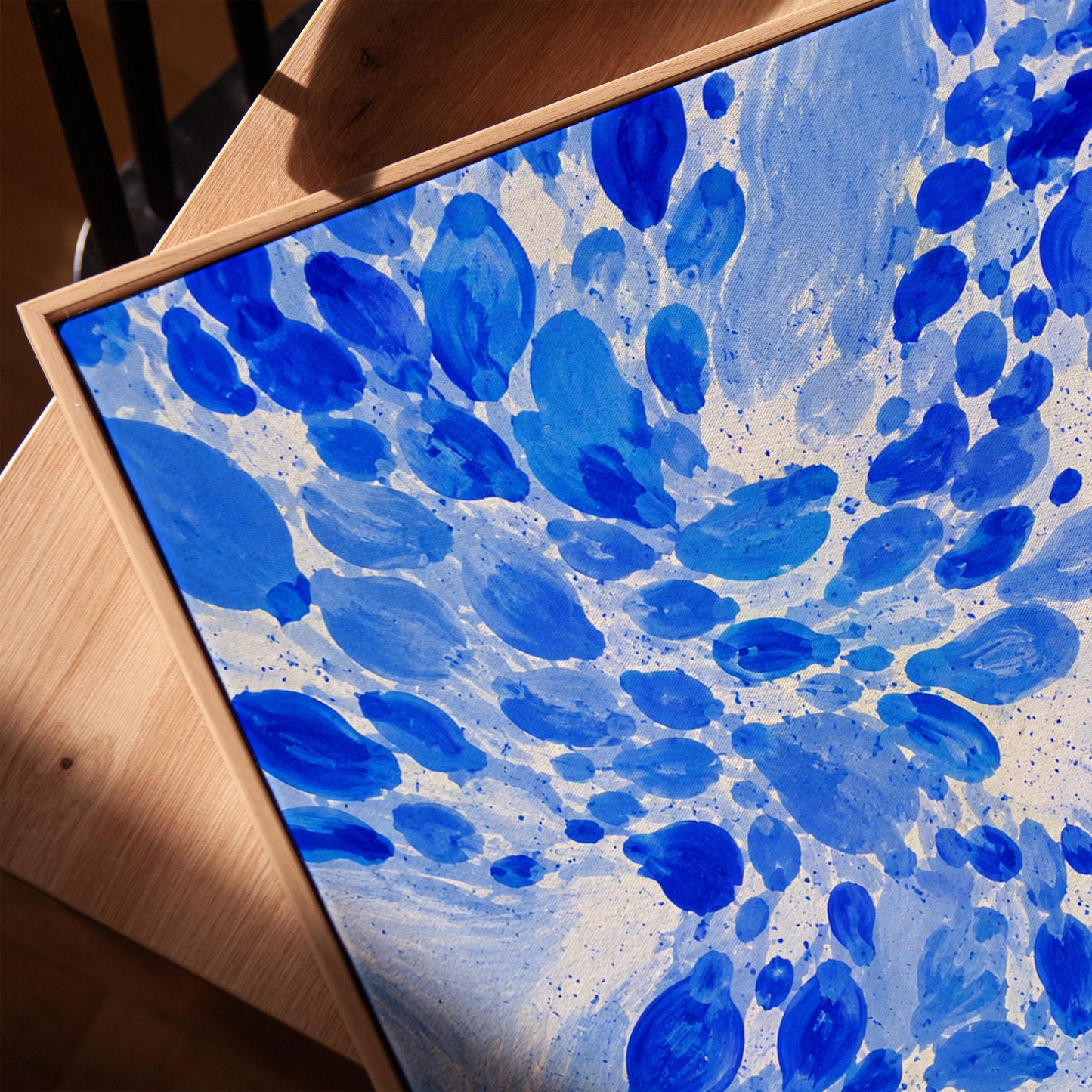 Burst of cobalt blue droplets scattering across pale background, canvas print in a warm, minimally styled interior