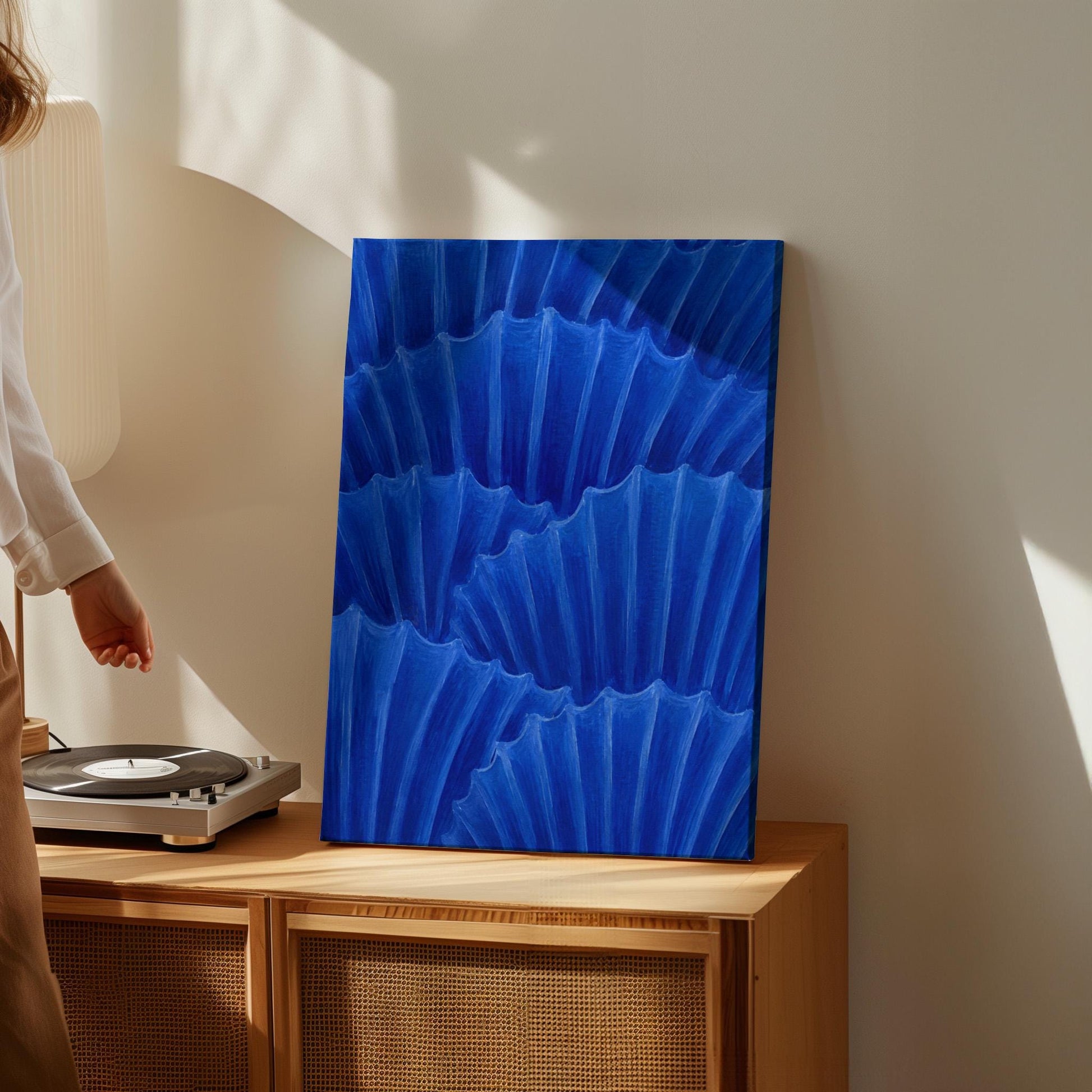 Overlapping pleated fan shapes in deep royal blue, canvas print hanging in a calm, modern living space