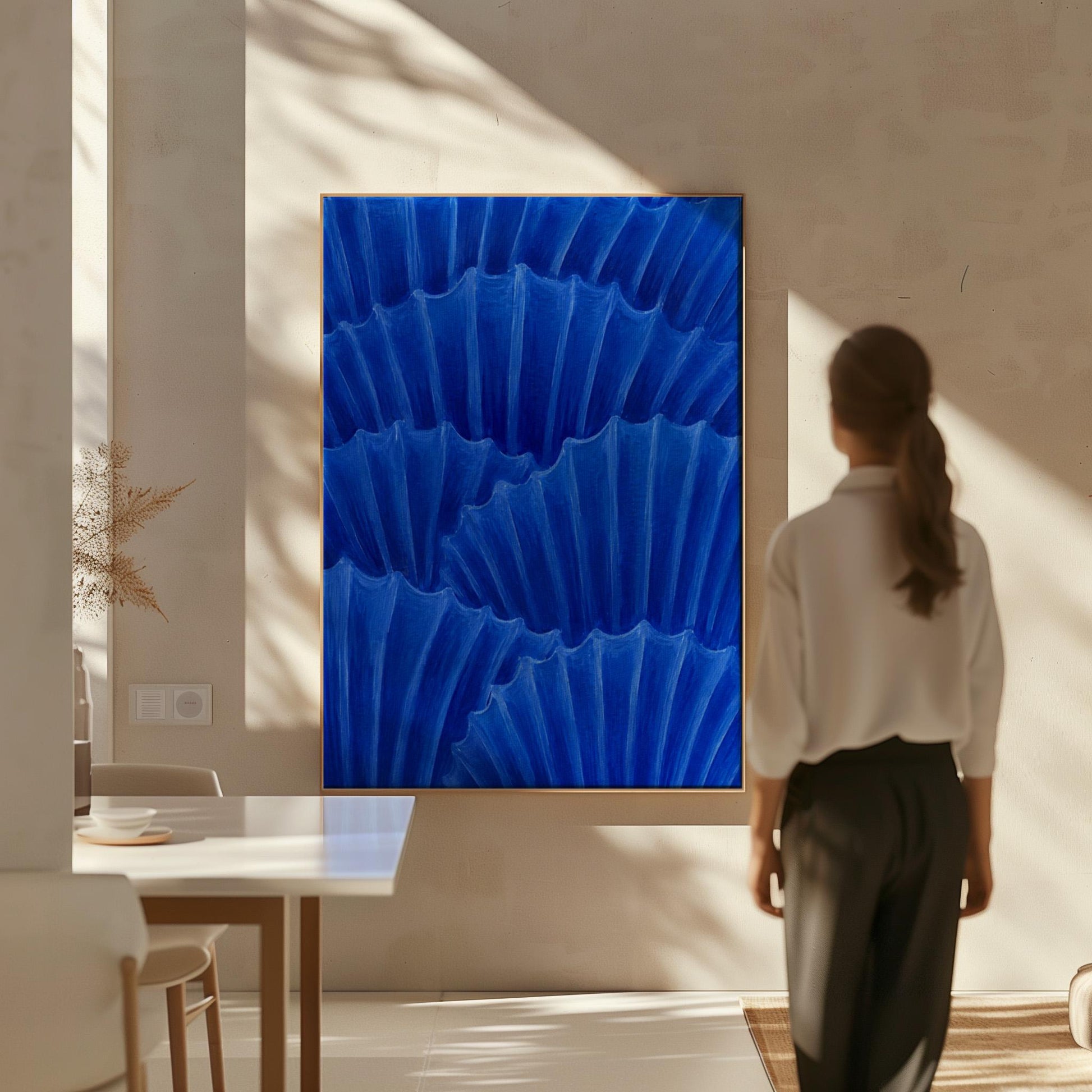 Overlapping pleated fan shapes in deep royal blue, canvas wall art hanging in a calm, modern living space