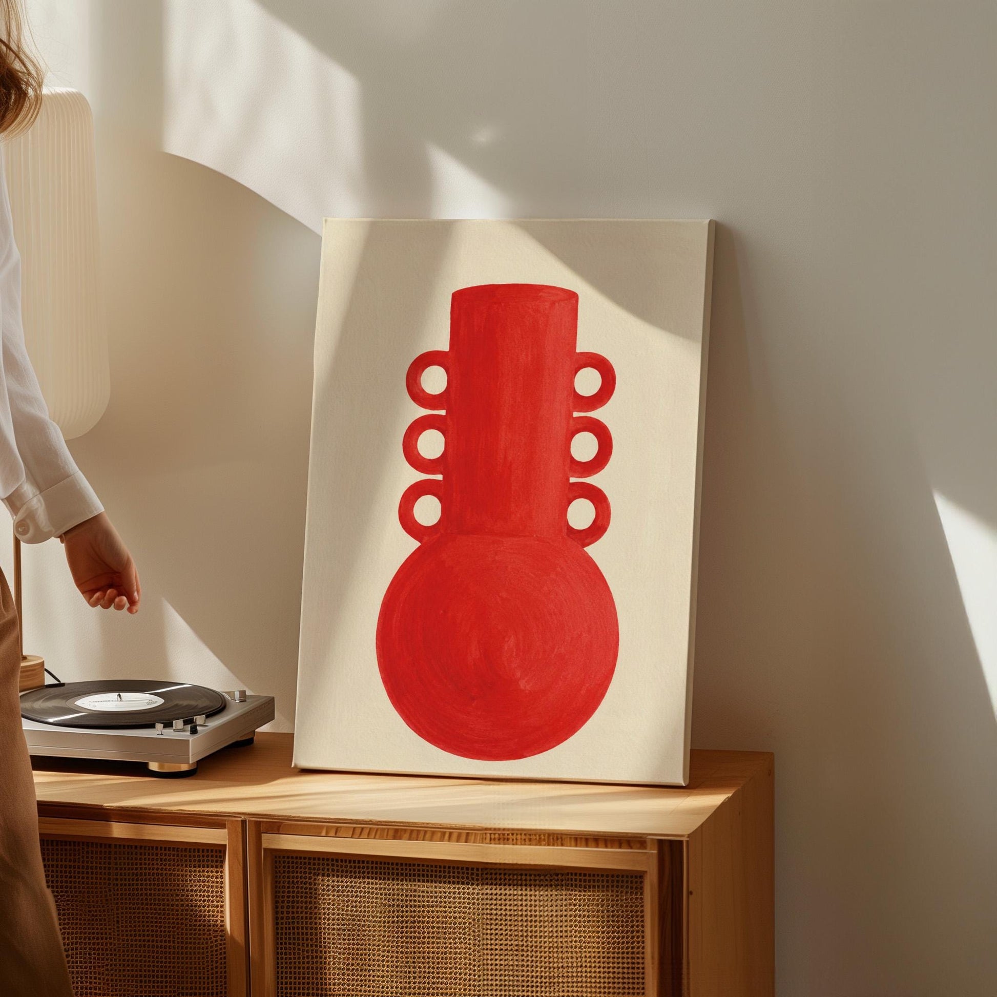 Bold red vessel with ring handles on cream background, canvas print shown to scale in a furnished room