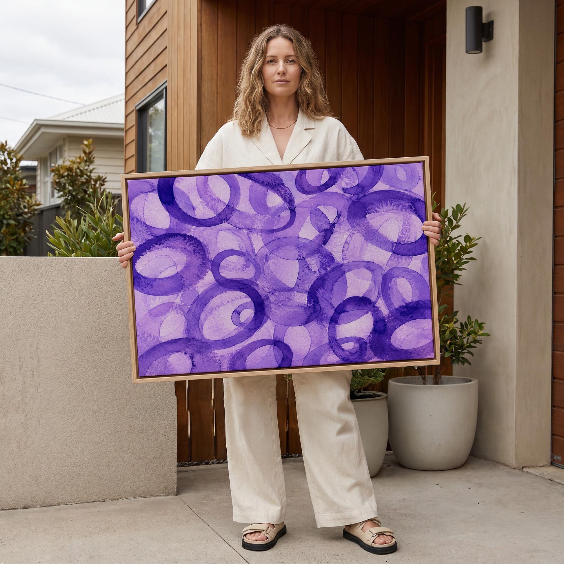 Swirling violet watercolor rings across wide frame, canvas wall art seen in a warm interior with natural light