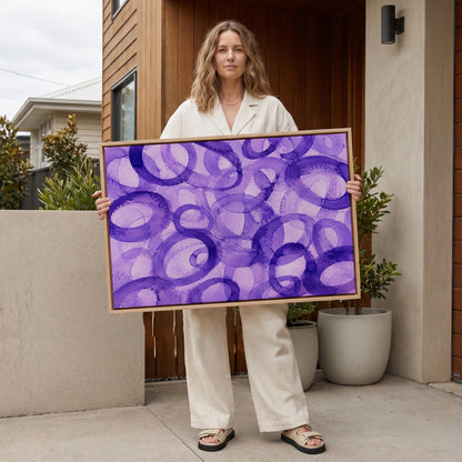 Swirling violet watercolor rings across wide frame, canvas wall art seen in a warm interior with natural light