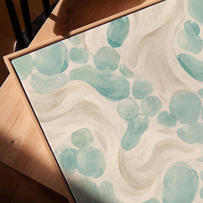 Aqua pebble shapes drifting among soft cream waves, canvas print in a warm, minimally styled interior