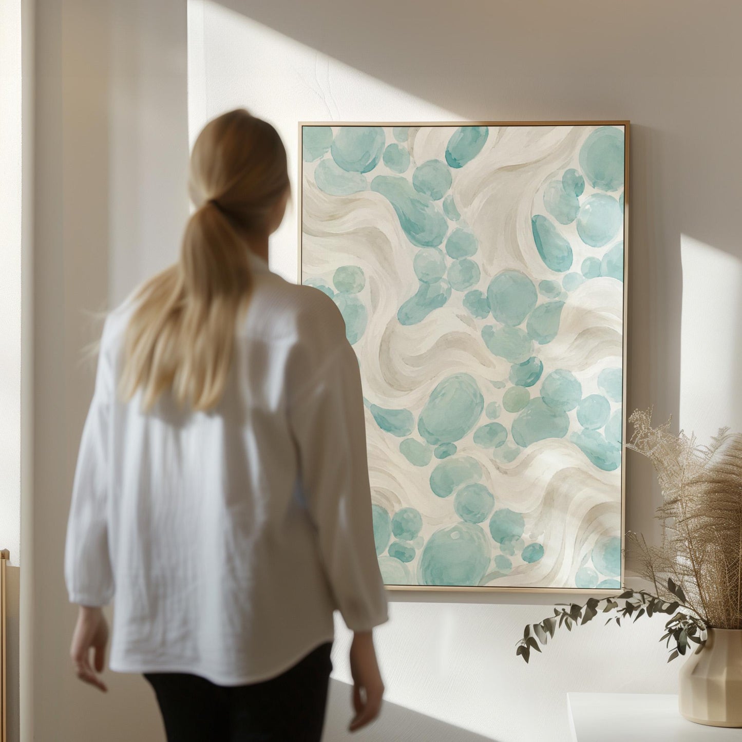Aqua pebble shapes drifting among soft cream waves, canvas wall art seen in a warm interior with natural light