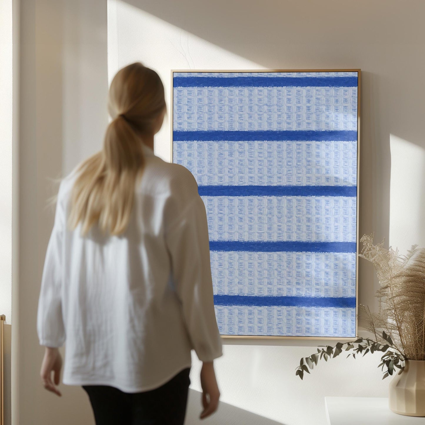 Bold cornflower blue stripes on a pale blue background, canvas wall art seen in a warm interior with natural light