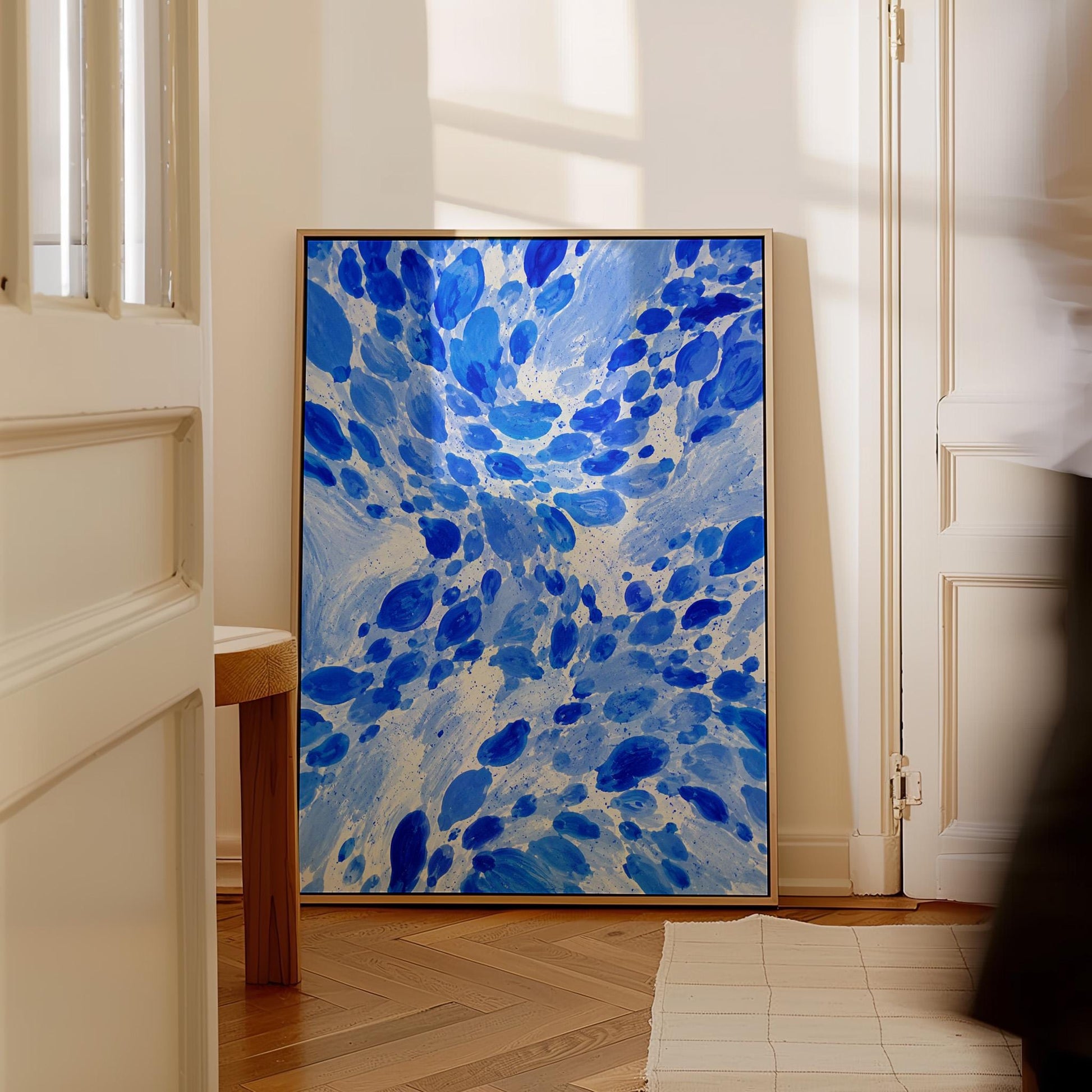 Burst of cobalt blue droplets scattering across pale background, canvas print shown to scale in a furnished room