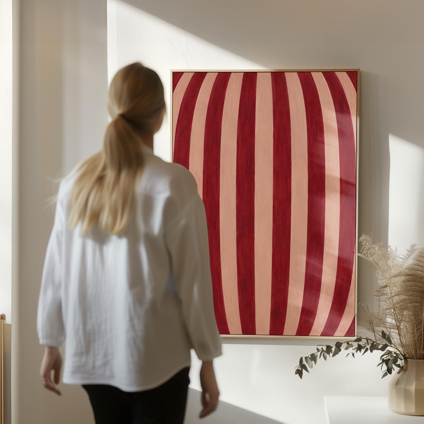 Curved burgundy stripes bowing over blush background, canvas print seen in a warm interior with natural light