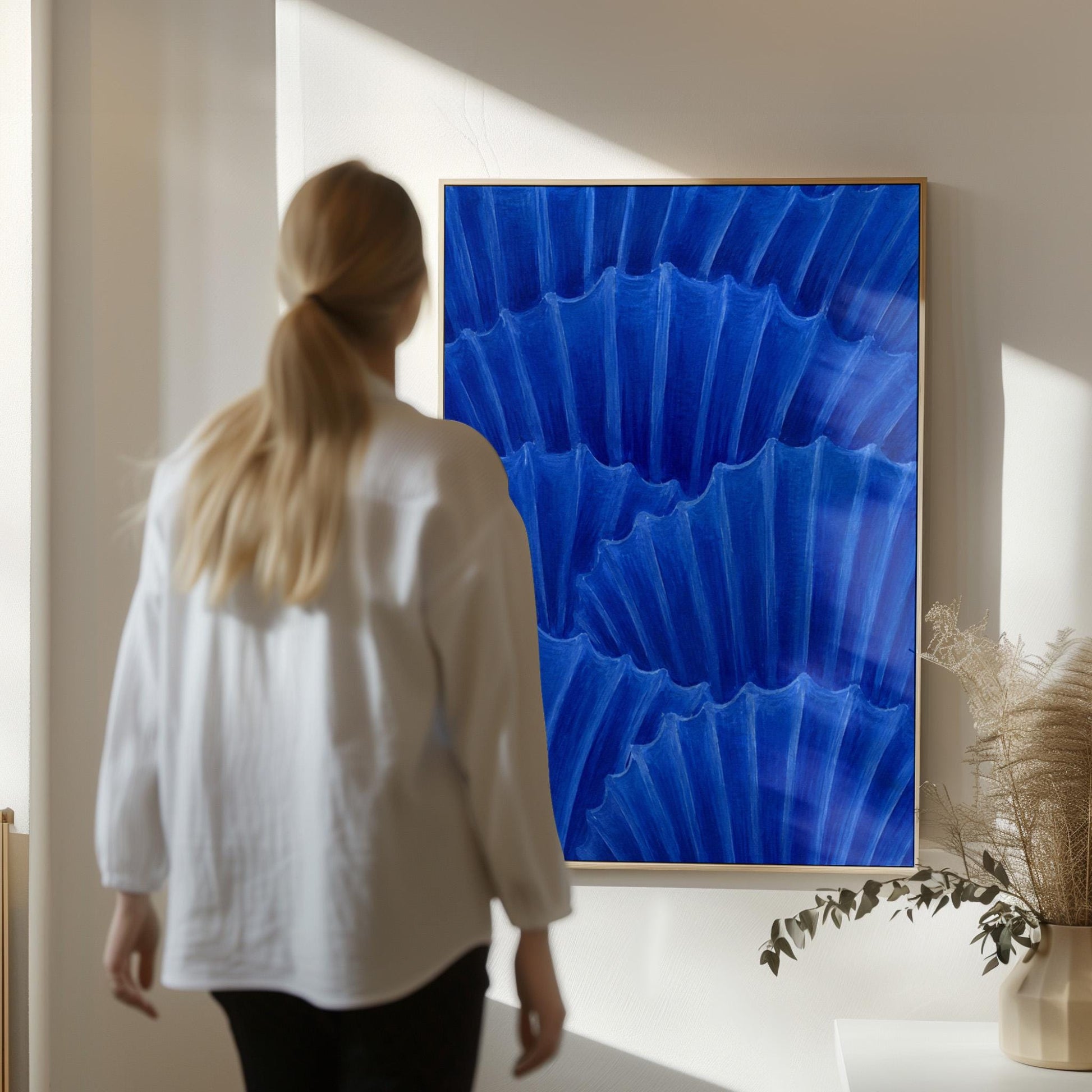 Overlapping pleated fan shapes in deep royal blue, canvas print displayed on a neutral wall in a styled interior
