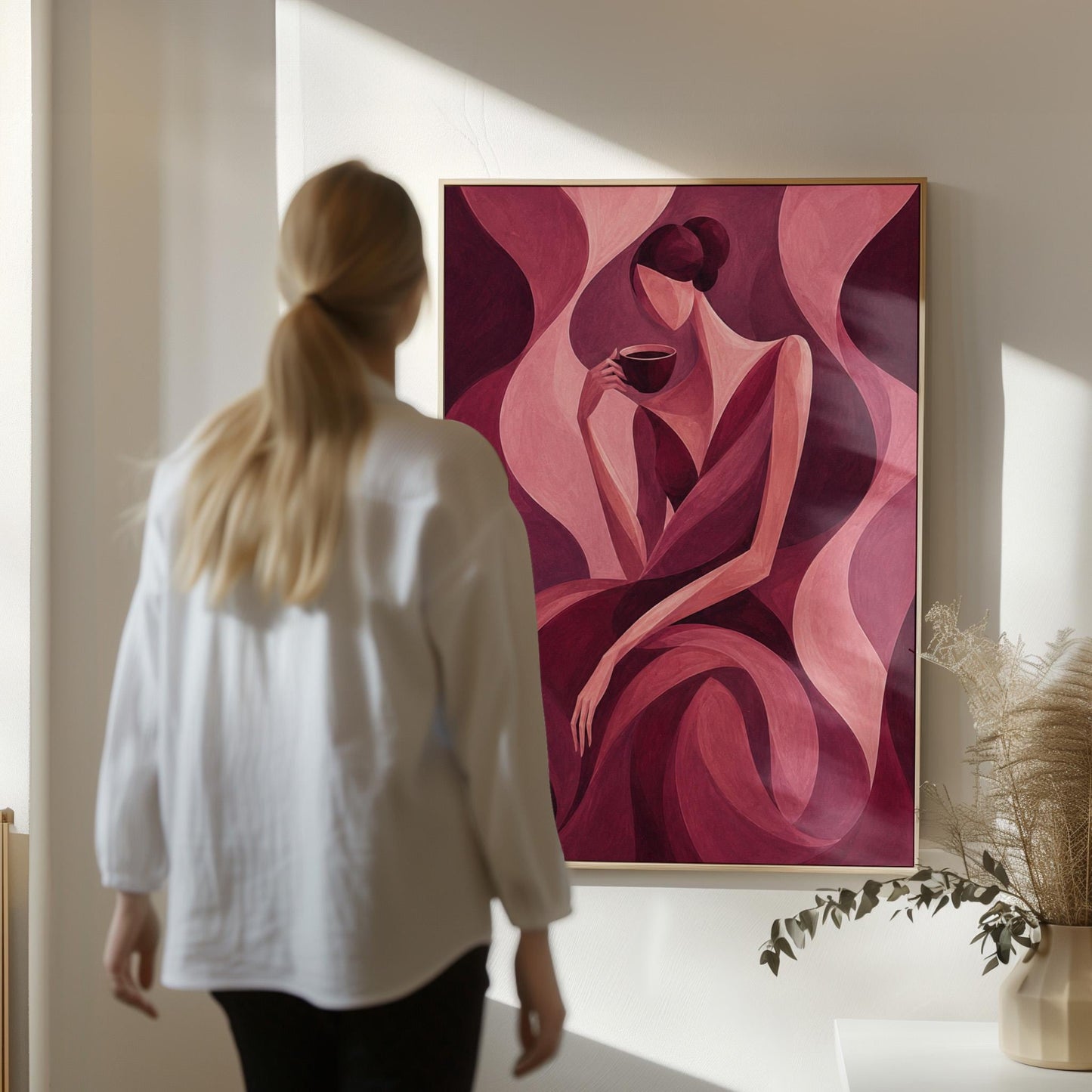 Woman sipping coffee among soft burgundy waves, canvas print hanging in a calm, modern living space